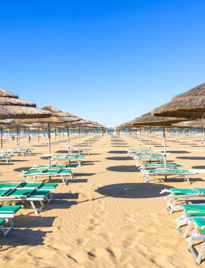 Spiaggia con lettini e ombrelloni di paglia, cielo limpido.
