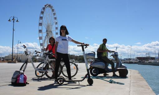 Personen mit Fahrrädern, Roller und Moped nahe einem Riesenrad.