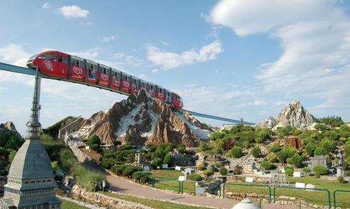 Treno sospeso sopra un parco con miniature di montagne e edifici.