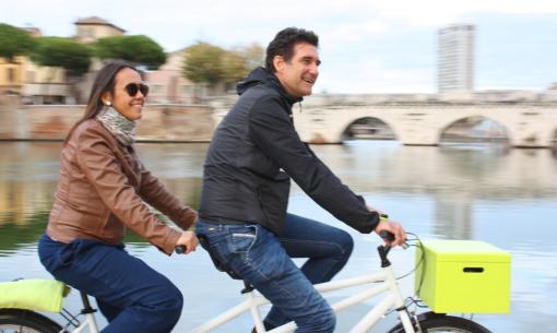Coppia in bici davanti a un ponte storico, giornata serena.