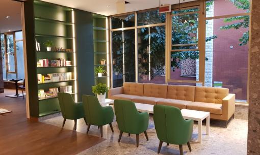 Salon moderne avec bibliothèque, canapé beige et fauteuils verts.