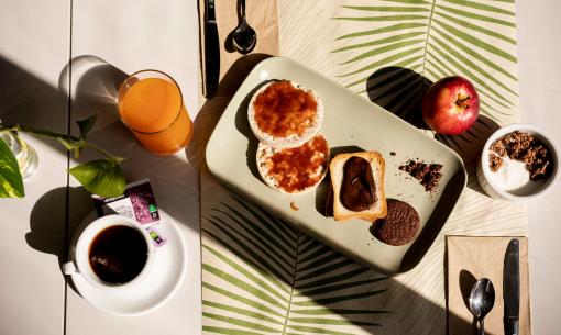 Colazione con tè, succo, pane, marmellata, cioccolato, mela e yogurt con cereali.