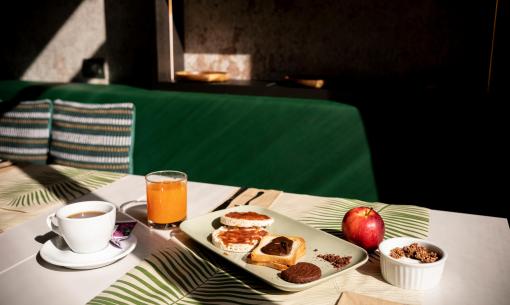 Petit-déjeuner avec thé, jus, toast, pomme et yaourt aux céréales.