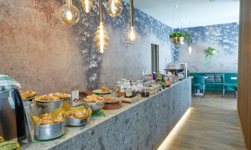 Buffet di colazione con croissant, marmellate e bevande in un ambiente accogliente.
