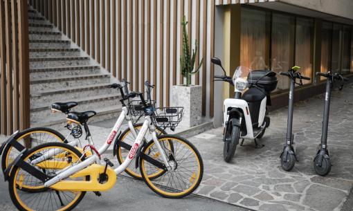 Biciclette e monopattini elettrici accanto a uno scooter, atmosfera urbana e moderna.